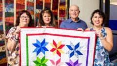 Administrative Assistant Joy Ruhl, Dean Kathleen Weigel, Assistant Professor Joseph Melita, and Assistant Professor Brittany Kiser show off one of Weigel's quilts inside the College of Education.