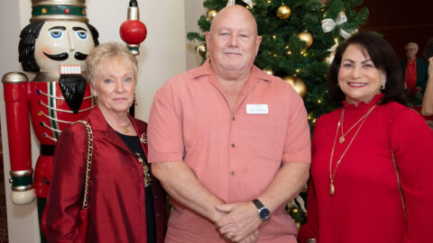 Marilyn and Ben Heyward and Linda Melcer pose in front of a Christmas tree.
