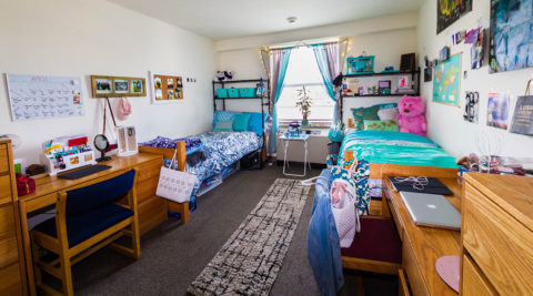 Two blue twin beds and two desks inside a dorm room in Trinity Residence Hall.