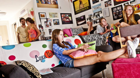 Students sit on a bed and couch while watching TV in E.M. Lynn Residence Hall.