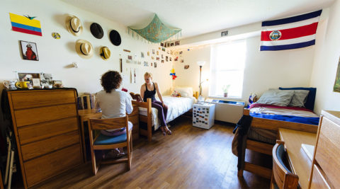 Two students hang out inside a dorm room in the de Hoernle Residence Hall. Two twin beds, desks, dressers and students' decorations are featured.