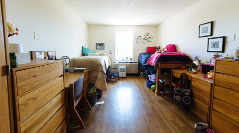 Dorm room in Freiburger Residence Hall with two twin beds, two desks with chairs, two dressers, a window and wall art.