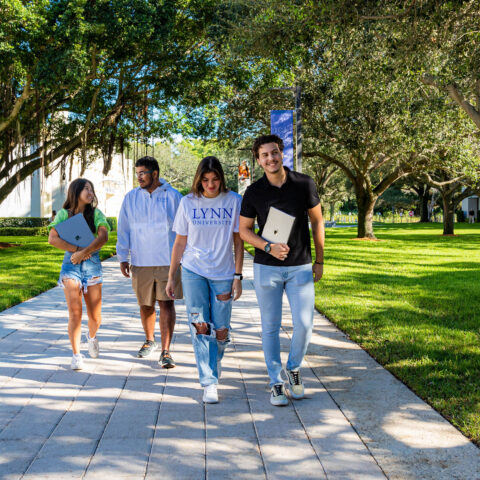 Four students walk through campus with trees in the background.