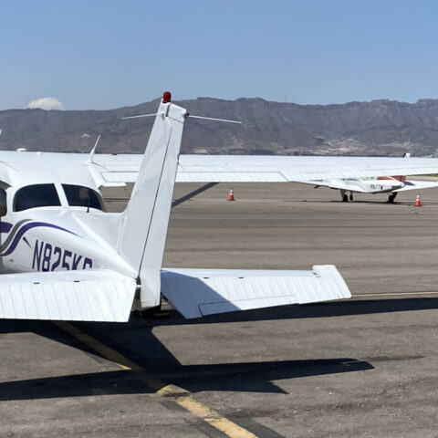 Flight instructors Blaise DaCosta, Jensen Kervern, and Marisa Vietti take a picture of a large silver airplane with mountains in the backdrop.