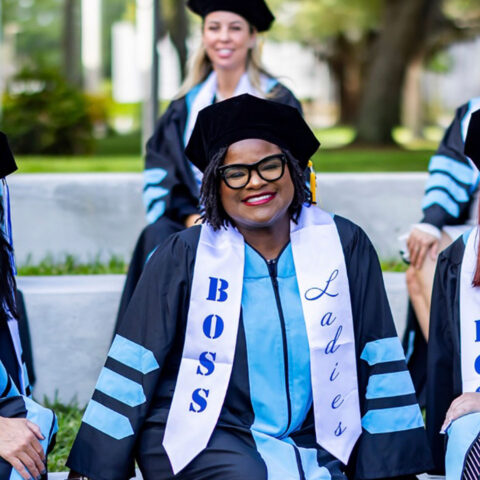 Dcotoral graduate boss ladies group photo with three sitting and three standing in their graduation cap and gowns.