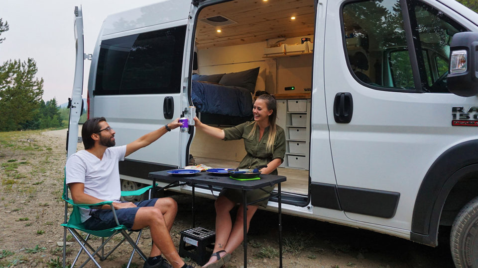 Christian and Kayla Manzano cheers each other at a table outside their campervan.