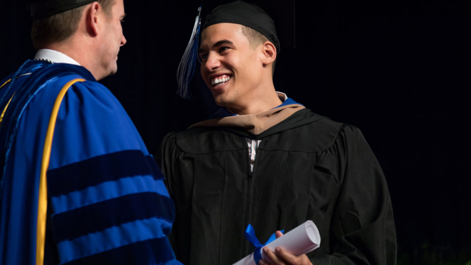Student receives diploma from President Ross at graduation.