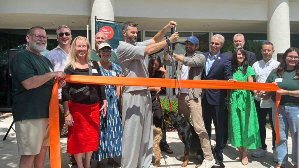 Brett Podolsky, Mayor Scott Singer and economic development team join together for a group photo cutting an orange ribbon in front of The Farmer's Dog's new office.