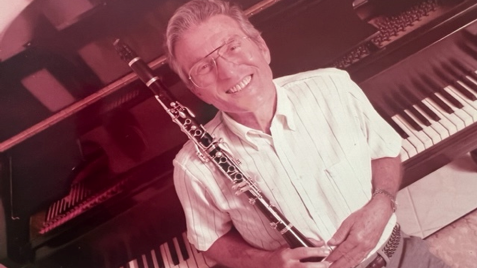 Marshall Turkin holds a clarinet while sitting at the Steinway & Sons piano.