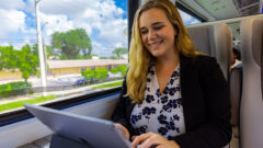 Online student smiles while she uses an iPad inside a Brightline train.