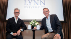 Bruce Himelstein and Ken Rehmann smile as they sit on stage at Elaine's with the Lynn logo in the backdrop.