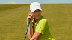 Victoria wears her clothing brand while posing with a golf club outside.