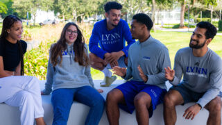 Five students wearing Lynn apparel sit together and laugh.