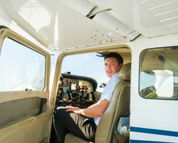 A student sits in the cockpit of a plane with the door open.