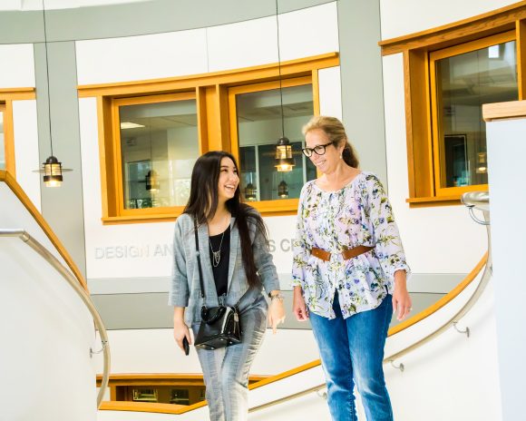 A student and a teacher walk up the stairs toward the College of Communication and Design.