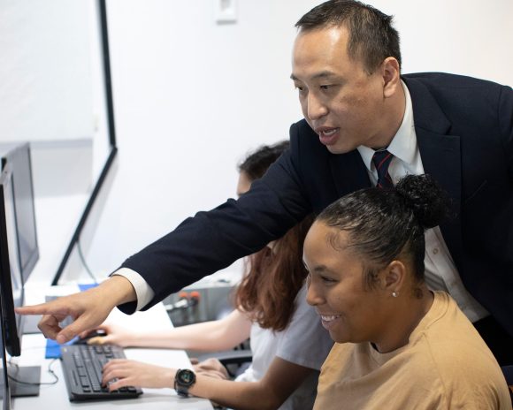 Professor helps student on the computer in a master's class.