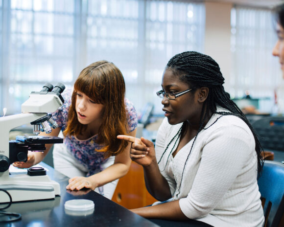 Two female students prepare a microscope in the science lab