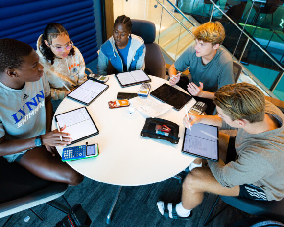 A group of students sit around a table in the university center and work on a project.