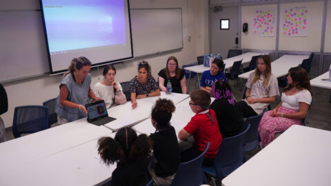 Students gathered around a table to watch presentation on an iPad.