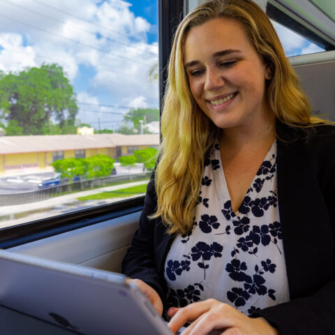 Online student smiles while she uses an iPad inside a Brightline train.