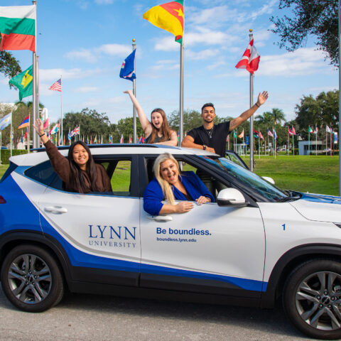Staff members inside a Lynn vehicle wave with smiles in front of the Circle of Flags.