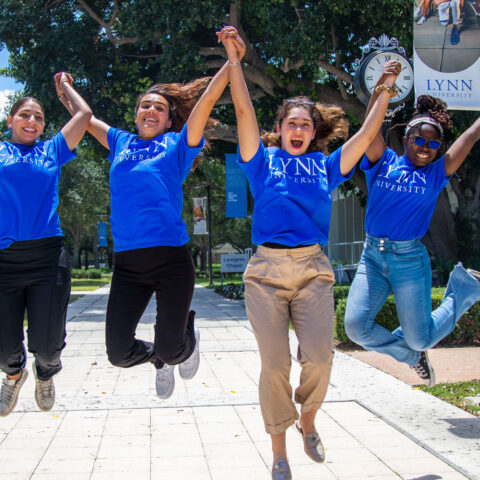Four girls wearing Lynn University shirts jump with excitement.