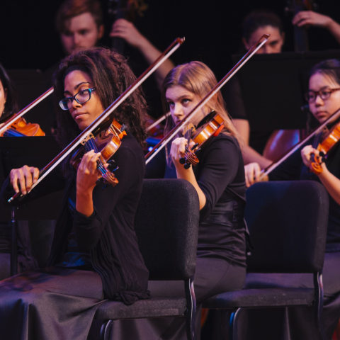Students play their string instruments in a concert.