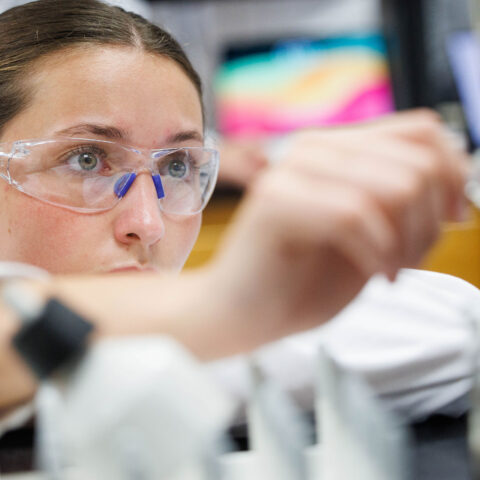Female student has protective glasses in a science classroom using a beaker.