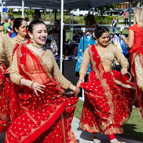 Bollywood dancers in red dresses march with smiles during Lynn's parade of flags.