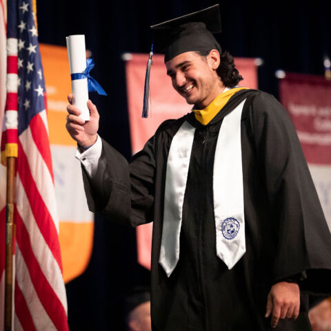 Student walking across the stage at graduation holding up a diploma