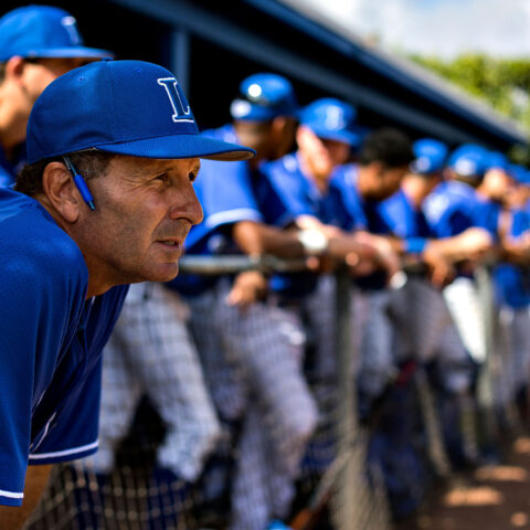 Rudy Garbalosa leans forward in the dugout with his team in the background.
