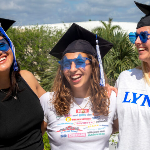 Three students wearing graduation caps and blue sunglasses pose for the camera.