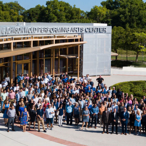 Faculty and staff stand together and take a photo outside the Wold Performing Arts Center.