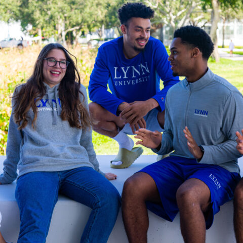 Five students wearing Lynn apparel sit together and laugh.