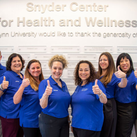 Snyder Center for Health and Wellness staff members stand in front of a wall with their thumbs up.