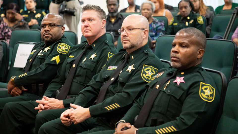 The BSO graduation cohort II sit in a conference room during the ceremony in their uniforms.