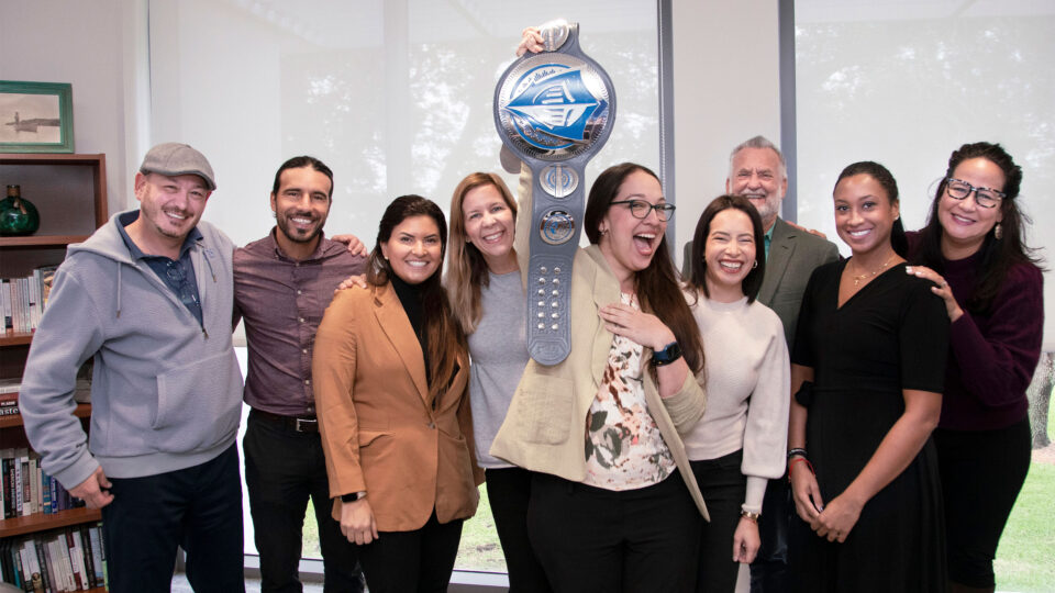 November 2023 Employee of the Month, Antonella Regueiro, stands with other Lynn faculty and staff members and holds the EOTM belt.