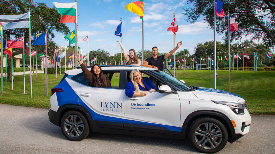 Staff members inside a Lynn vehicle wave with smiles in front of the Circle of Flags.