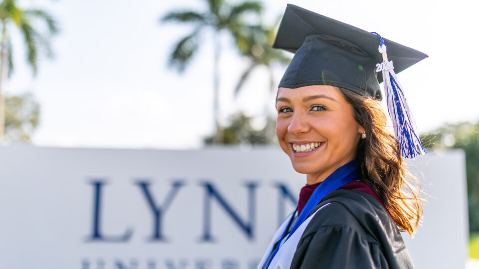 A graduate poses for the camera in front of the Lynn sign.