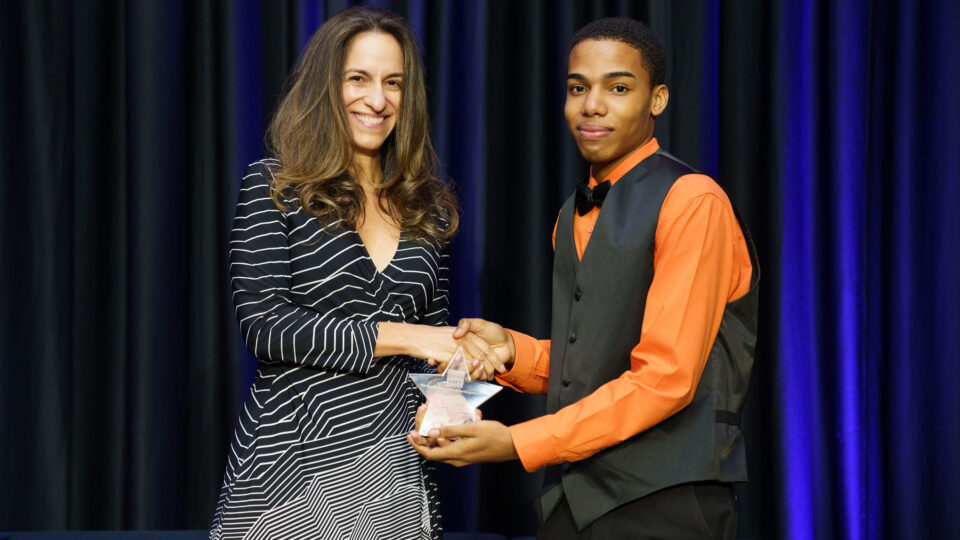 A representative hands a small trophy award to a student.