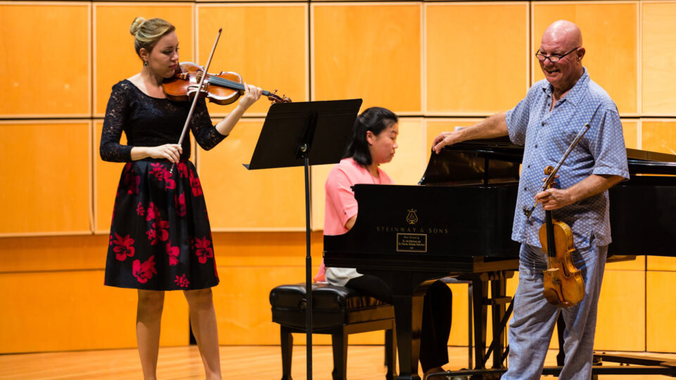 Elmar Oliveira on stage with a conservatory of music student playing the violin during a rehearsal..