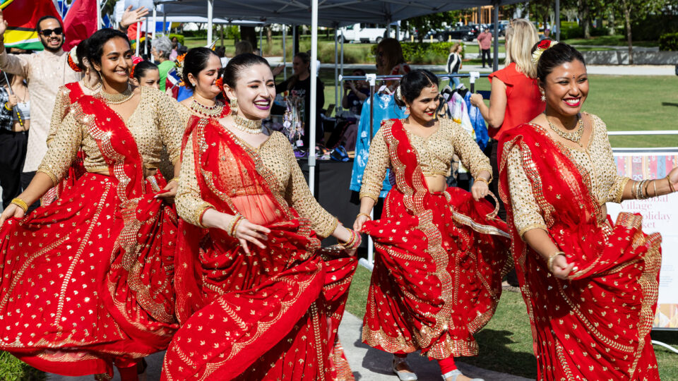 Bollywood dancers in red dresses march with smiles during Lynn's parade of flags.