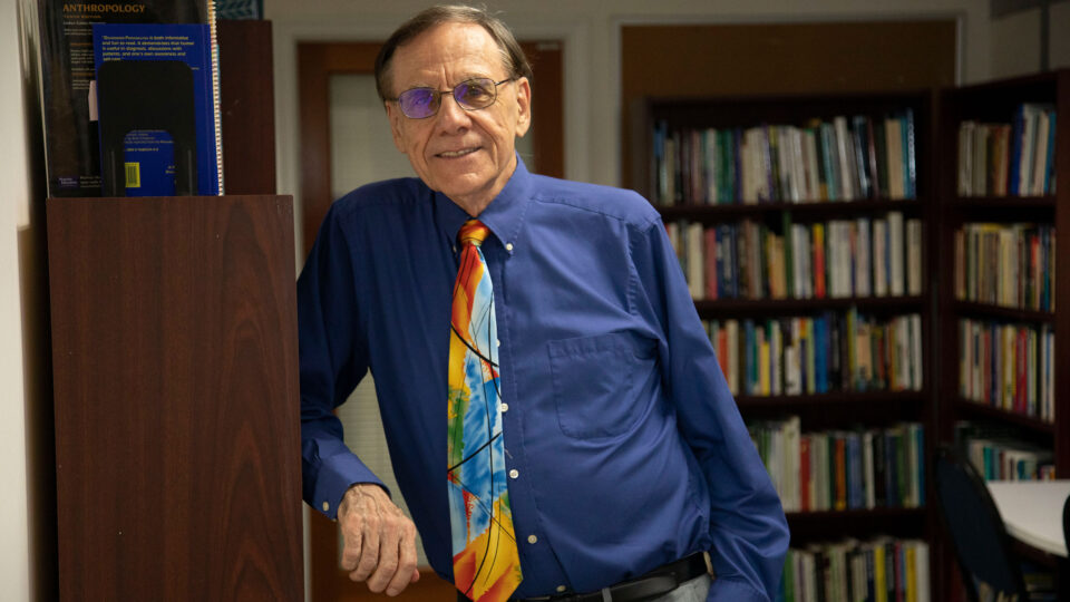 Dr. Len Sperry smiles in front of a library of books