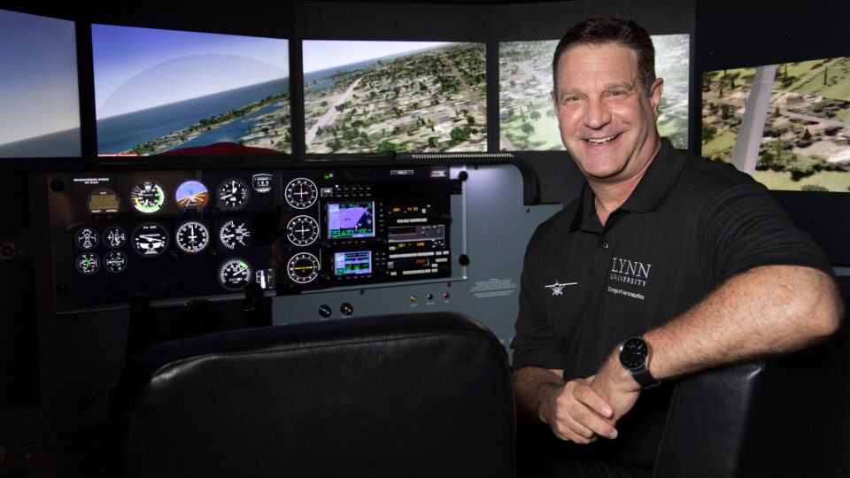 David Cohen, dean of aeronautics, smiles in front of a flight simulator cockpit