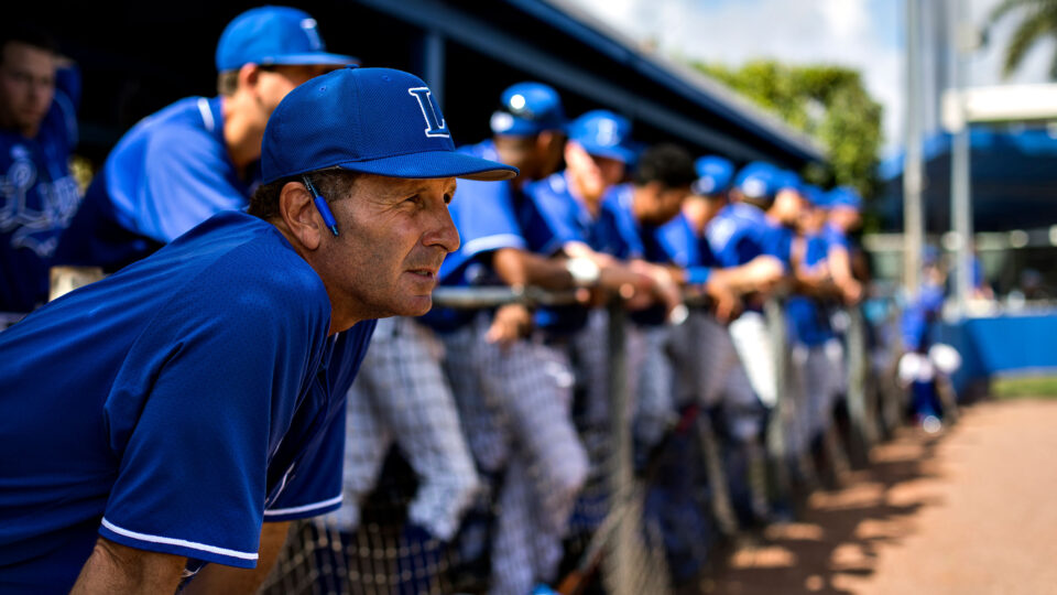 Rudy Garbalosa leans forward in the dugout with his team in the background.