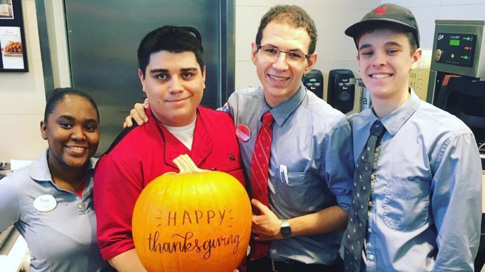 Alumn Shawn Johnson smiles with group of young employees from Chick-Fil-A as they hold a Thanksgiving pumpkin.