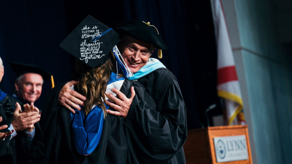 Dr. Dan Bagnoni hugging female student on commencement stage