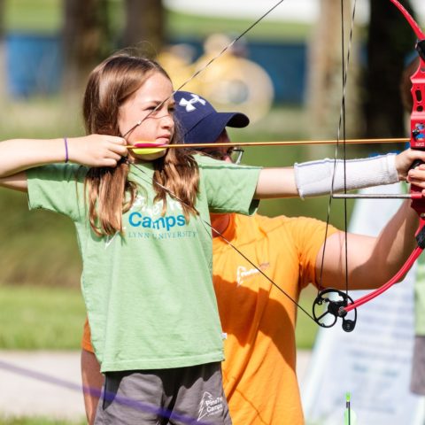 Girl shooting a cross bow with help of a counselor