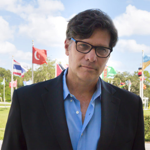 Dr. Robert Watson in front of flags on Lynn campus